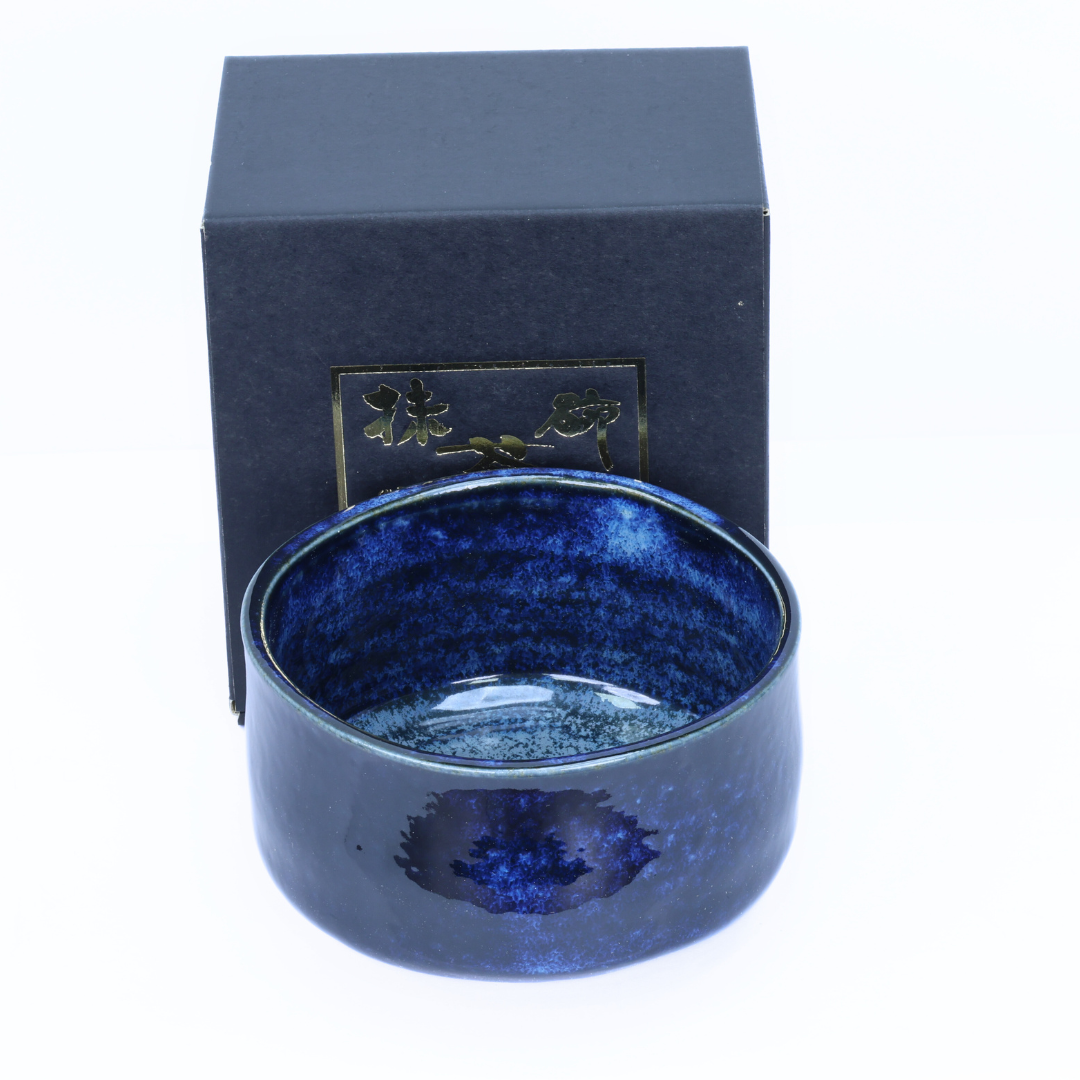 Blue porcelain matcha bowl with textured interior in front of a matching box on a white background